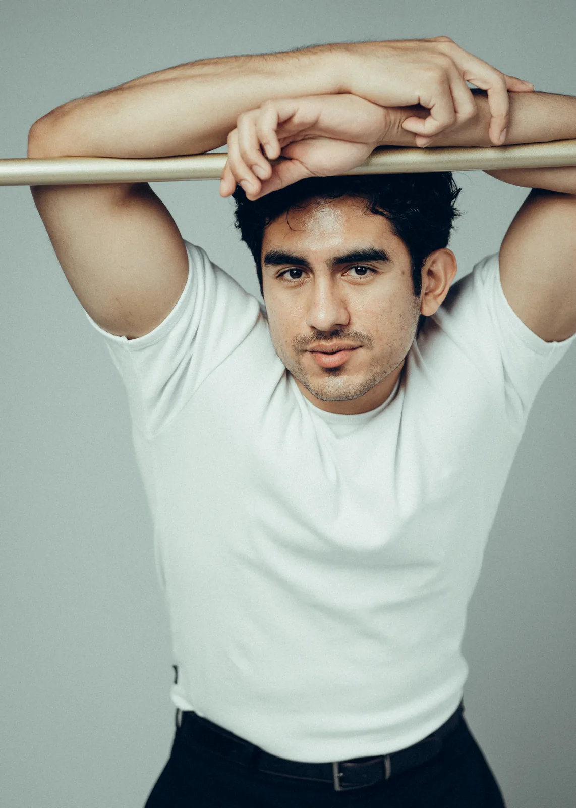 Lenny Ramos studio portrait, arms resting overhead on a barre